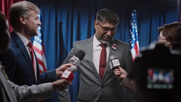 カリスマ的なインド系アメリカ人の男性大統領候補者にインタビューし 選挙プログラム 移民政策について質問するマイクとカメラを持つ多民族ジャーナリストの中間ショット — ストック動画