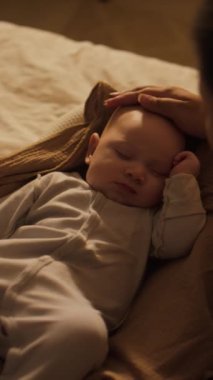 3 aylık vücut giysisi giymiş, geceleri kozanın içinde uyuyan bir çocuğun dikey omuz üstü fotoğrafı ve tanınmayan bir anne nazikçe kafasını okşuyor.