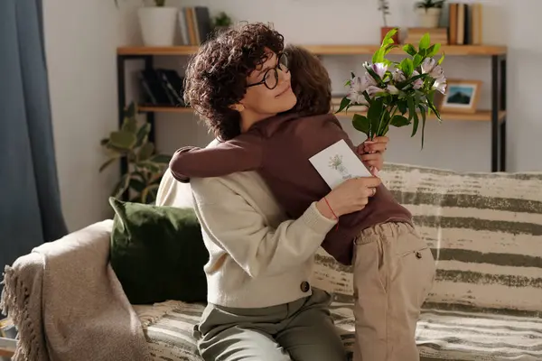 stock image Affectionate boy embracing his smiling mother with handmade postcard in hand while congratulating her on traditional holiday