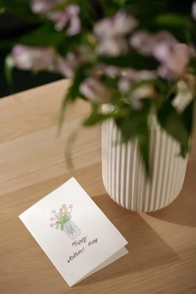 有一张木制桌子 上面有手工制作的明信片 上面印有对母亲节的问候 并在花瓶里画了一束红色郁金香 — 图库照片