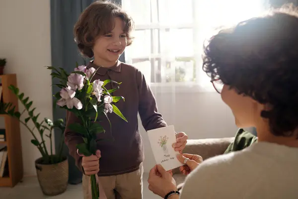 快乐可爱的男孩拿着一束鲜花把手工制作的贺卡递给他的妈妈 同时在传统的春节假期向她表示祝贺 — 图库照片