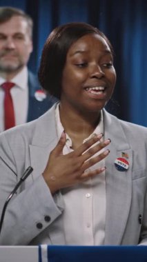 Genç Afrikalı Amerikalı kadın politikacının ABD Cumhuriyetçi ya da Demokrat Partisi 'nden başkanlık adaylığı kampanyası için sahneden, konuşmadan, el sallayarak seyircilere seslenişinin orta boy dikey çekimi.