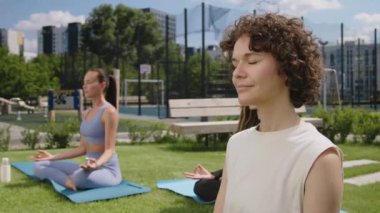 Kafkasyalı sakin, kıvırcık saçlı kadının grup yogası sırasında şehir çatısı parkında gözleri kapalı meditasyon yaparken görüntülerini çek.