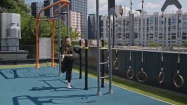 Modern çatı spor salonunda güzel şehir manzarasıyla egzersiz yapmadan önce siyah spor elbiseli bayan sporcunun bacak ve eklemlerini esnetme ve ısıtma görüntüleri.