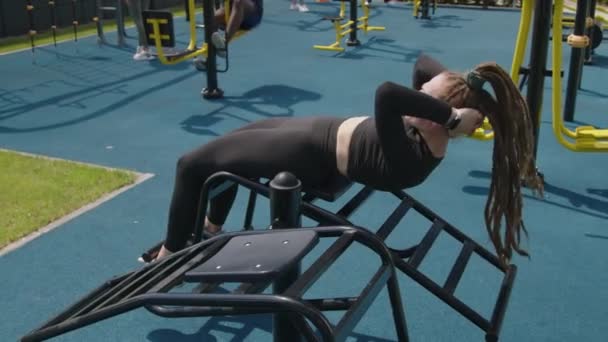 スポーツグラウンドで運動機器の上に座ったり クラッチしたりする女性のサイドフルビデオ — ストック動画