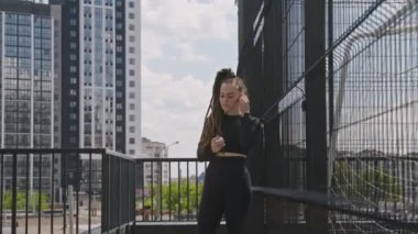 Rastalı kadın koşucunun orta bölüm görüntüleri. Kulaklık takıp müzik çalıyorlar. Sonra da çatıda koşmaya devam ediyorlar.