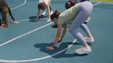 Çeşit çeşit sporcuların güneşli bir günde çatıdaki spor sahasında yaptıkları burpee egzersizlerinin yan görüntüleri.