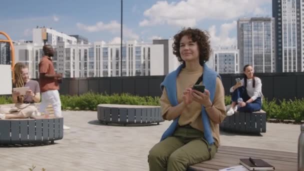 現代の屋根公園のベンチネアのビジネス文書に座っている携帯電話にメッセージを送信する白人女性の完全な映像 — ストック動画