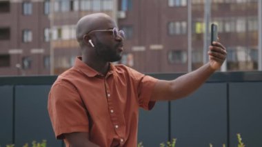 Afrika kökenli Amerikalı iş adamının dışarıda otururken, güneş gözlüğü ve kulaklıkla vedalaştığı ve cep telefonu kullandığı video görüntüleri.
