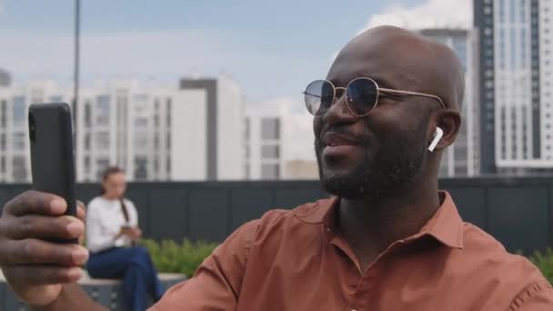 Güneş Gözlüklü Kulaklıklı Afro Amerikan Bir Adamın Telefon Ekranına Baktığı — Stok video