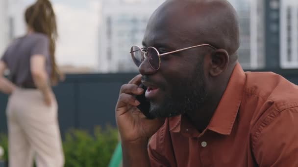 여름날 공원에 앉아있는 전화에 대화를하는 선글라스에 아프리카계 미국인 남자의 클로즈업 — 비디오