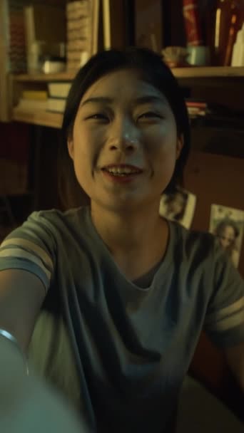 拍下了一张照片 照片中带着微笑的亚洲女孩与朋友或家人在智能手机上进行视频通话 一边挥手 一边分享消息 一边笑着 一边在晚上的小寝室里坐着 — 图库视频影像