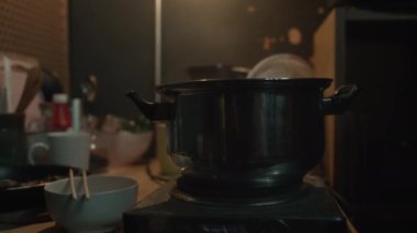 Orta ölçekli hiç kimse küçük elektrikli ocakta haşlama tenceresi, yemek çubuklarıyla kase, yemek ve çanak çömlek ile kızartma tavası Çin 'de ya da Hong Kong' da loş bir kapsülde masada çekilmez.