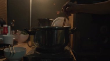 Tanınmayan birinin orta ölçekli fotoğrafı, Çin 'de küçük, karanlık bir dairede, yemek çubuklarıyla dolu bir kase içinde buharda pişen bir şeyi karıştırıyor.