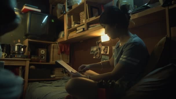 中全镜头 年轻的韩国或中国女人坐在双层床上 靠在小公寓里的枕头上 用铅笔画东西 同时在电炉上用平底锅做饭 — 图库视频影像