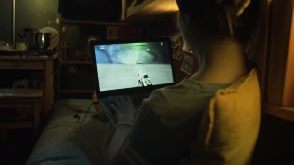 傍晚时分 隐姓埋名的年轻女性坐在凌乱的鞋盒中躺在床上 在笔记本电脑上玩射击视频游戏 通过水平 — 图库视频影像