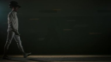 Eskrim pistine gelen, miğfer takan ve yarışmadan önce ya da karanlık salondaki eğitim sırasında folyo kılıcını kaldırırken başlangıç pozu alan erkek folyo eskrimcisinin tam görüntüsü.