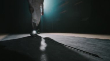 Zemin seviyesinde, karanlık salonda kılıç kullanırken tanınmayan bir eskrimcinin Folyo kılıcını eline alışının görüntüleri.