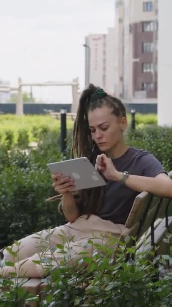 白种人带着恐惧的头发 穿着休闲装 在平板电脑上远程工作 坐在空公寓屋顶公园的木制长椅上的垂直侧影 — 图库视频影像