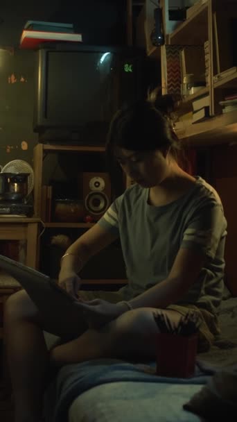 靴箱の平らなまたは寮の二段ベッドに座っているカジュアルな服の若い中国の少女の完全な縦のショットは 電気ストーブで夕食を調理しながら スケッチブックで静物の絵を描きます — ストック動画