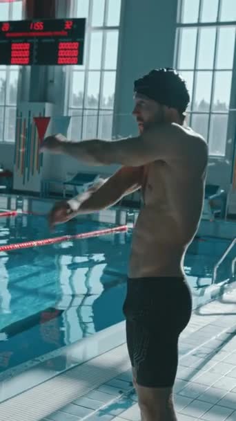 白种人男子体格健壮 头戴泳帽 身穿泳裤 站在游泳池边 做热身运动 摆动手臂准备练习的中式垂直射击 — 图库视频影像
