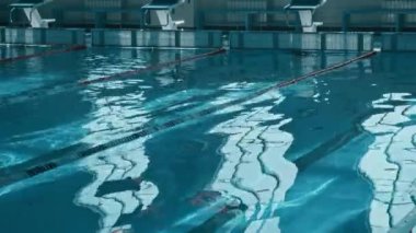 Yüzme havuzunun derin ucunda dalış bloklarından ve dalgalanan turkuaz su yüzeyinden çekilen hiç kimse yok. Gündüz vakti camların çarpık yansımaları ve skorborda kırmızı harfler var.