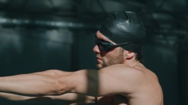 Yüzme gözlüklü genç erkek triatlon sporcusunun orta boy yakın çekim görüntüleri, kauçuk başlıklı, dönen omuzlu, kollarını esneten, bilardo antrenmanına hazırlanırken