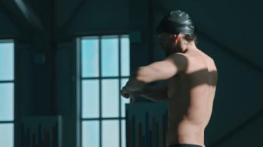 Genç sporcunun bel dönüş egzersizi yaptığı, sonra eğilip dalış bloğuna tutunduğu ve yüzme havuzu antrenmanına hazırlanırken vücut kaslarını esnettiği orta eğik bir yan çekim.