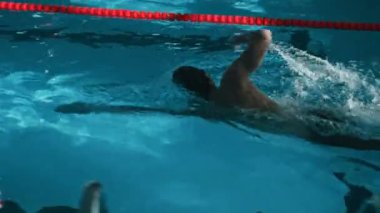 Siyah şortlu, kep ve gözlüklü, tanınmayan bir sporcunun havuz, spor salonu ya da natatorium şeridinde yüzerken orta boy görüntüsü.