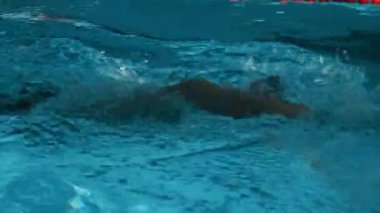 Siyah şortlu, kauçuk şapkalı ve gözlüklü kaslı sporcunun bilardoda ön şeritte yüzerken triatlon müsabakasına hazırlanırken orta boy yavaş çekimleri.