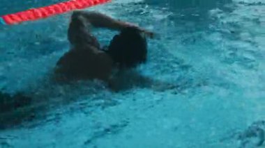 Siyah kauçuk şapkalı ve gözlüklü genç beyaz erkek sporcunun kırmızı şerit ayırıcıları boyunca serbest yüzerken yarışmanın bitiş çizgisine yaklaşırken orta yavaş görüntüsü.