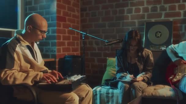 夜のレトロスタジオに座っている間 ギターとミディのキーボードで音楽を作成する白人女性と男性のミュージシャンの映像をパンニング — ストック動画