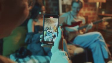 Telefon ekranında gitar çalan adamın ve stüdyoda şarkı yazarken imza atan kadının videolarına odaklı olarak.