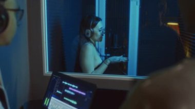 Arka planda iki erkek müzik yapımcısının neon ışıklı kabinde şarkı söyleyen kadın vokalisti izlerken şarkı kaydetme sürecinin tadını çıkardıkları görüntüler var.