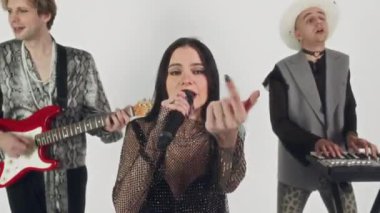 Glam rock grubunun beyaz arka planda grup halinde şarkı söyleyip, mikrofona şarkı söyleyen çekici beyaz vokalistinin görüntülerini aç ve kameraya bak.