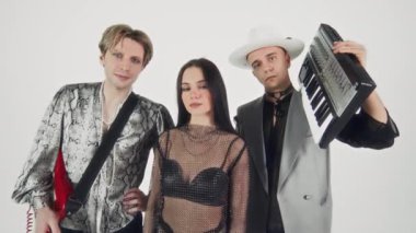 Beyaz arka planda mini sentezleyici ve elektro gitarla poz veren Kafkas glam rock bağımsız üçlüsünün portresini çıkar ve kameraya bak.