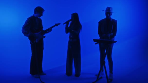 女性シンガーと男性ギタリスト キーボード奏者のシルエットの完全な映像 ブルーカラーネオンフィルターでプロのスタジオでギグ — ストック動画