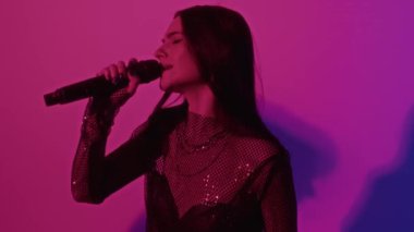 Pembe neon ışıklı stüdyoda çalarken bas gitaristle birlikte şarkı söyleyen kadın şarkıcının görüntülerini çıkar.