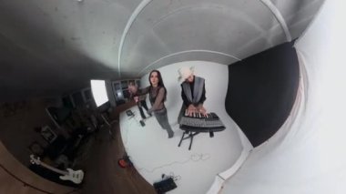 Kafkasyalı blogcu ve Glam Rock grubunun baş vokalisti, Stüdyoda gitar çalan basçı ve aksiyon kamerası 360 kullanarak sentezleyici çalan erkek klavyeciyi filme alıyor.