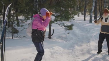 Sıcak kar giysileri ve yün şapkalar içinde, güneşli bir günde kayak yürüyüşü yaparken kış ormanlarında oynak kar topu savaşı yapan yaşlı beyaz karı ve kocanın yavaş çekimleri.