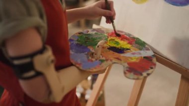 Yağ rengi fırça ve palet kullanan yapay kol boyalı kimliği belirsiz bir çocuğun yan kesit görüntüsü.