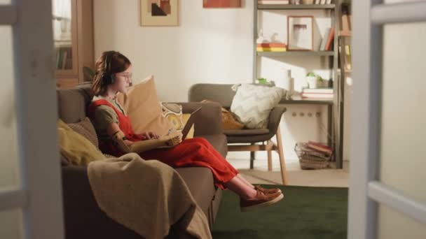 居心地の良いリビングルームでソファーに座っている間 ロボットアーム学習のロボットアームの女の子のサイドフルビデオ — ストック動画