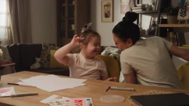 Orta ölçekli görüntülerde, beyaz anne Down sendromlu çocukla öpüşüyor ve oynuyor. Sanat terapisi sırasında keçeli kalem veriyor, gülümseyen büyükanne onları izliyor.