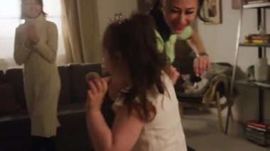 Anne ile oturma odasında oynayan, büyükannesinin onları izlediği ve alkışladığı, Down sendromlu, heyecanlı küçük bir kızın el kamerasıyla çekilmiş görüntüleri.