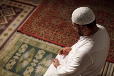 Olgun Müslüman bir adamın beyaz elbiseli, takiyeli, duacı halısında oturmuş namaz kılarken, kopyalama alanı yaparken yüksek açı görüntüsü.