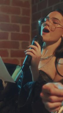 Beyaz kadın vokalistin şarkısını bitirdiği ve gitaristin eski tarz stüdyoda müzik kaydetmekten mutlu olduğu dikey görüntüler.