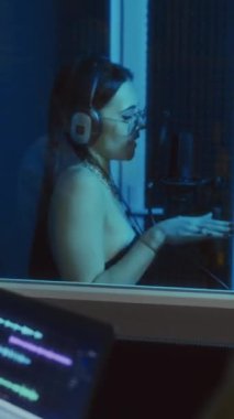 Kadın vokalist neon ışıklı kabinde şarkı söylerken, tanınmayan iki müzik yapımcısının şarkı kaydetme sürecinin keyfini çıkarırken dikey olarak çekilen görüntüler