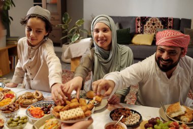 Mutlu Müslüman adam, kadın ve çocuk Uraza Bayram 'da aile yemeğinde yemek yerken tabaktan tatlılar alıyor.