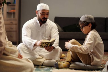 Sakallı Müslüman adam oturma odasında oturmuş aile toplantısında oğluna ve kızına Kuran 'ın anlamını anlatıyor.