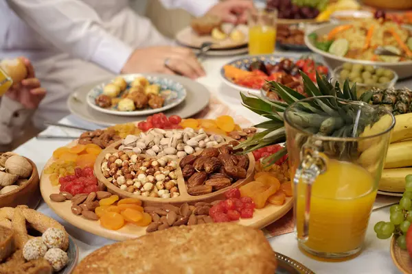 お祝いの食卓に甘い乾燥したフルーツとナッツの選択的な焦点ショット イードアルフィトを祝う認識できないイスラム教徒の人々 — ストック写真